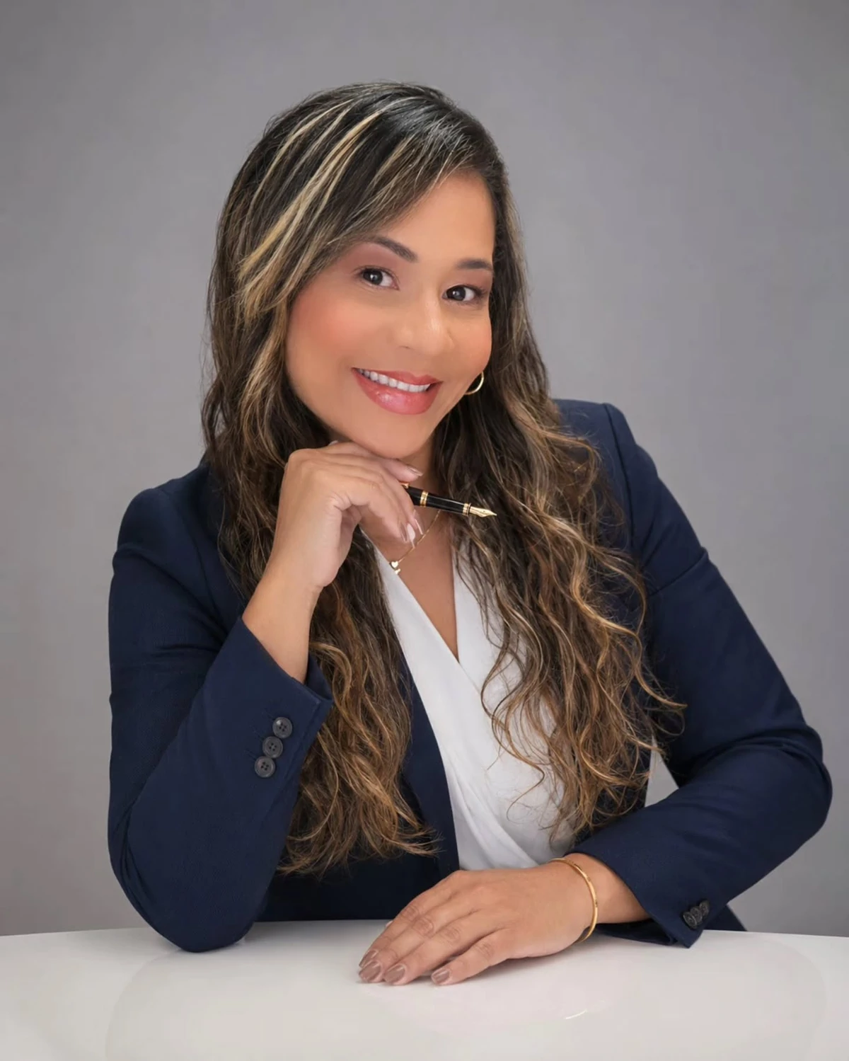 Joicelene Vieira, sorrindo, sentada à mesa em retrato profissional.